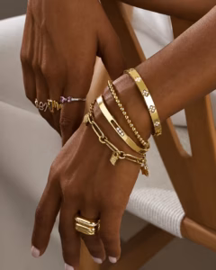 Stacked gold bangles, a diamond cuff and paperclip chain bracelets on a wrist