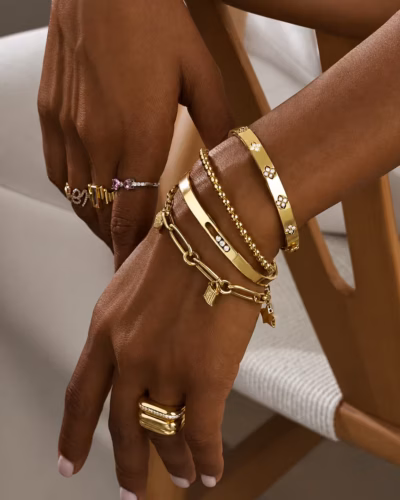 Stacked gold bangles, a diamond cuff and paperclip chain bracelets on a wrist